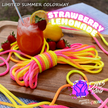 A bundle of bright neon-colored rope or cord wrapped in pink, yellow, orange, and blue stripes, styled on a wooden board with a drink, strawberries, lemons, and promotional text reading 'Strawberry Lemonade' and 'Dye the Band'.