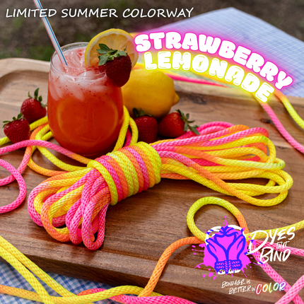 A bundle of bright neon-colored rope or cord wrapped in pink, yellow, orange, and blue stripes, styled on a wooden board with a drink, strawberries, lemons, and promotional text reading 'Strawberry Lemonade' and 'Dye the Band'.